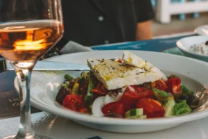 a bowl of greek salad and a glass of wine
